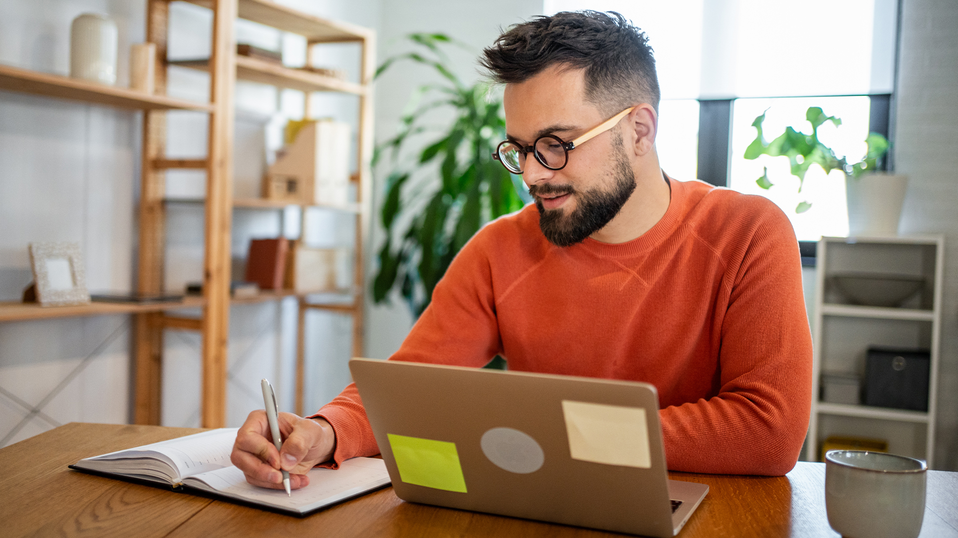 Man in his 30s working at his desk, wearing an orange sweater 