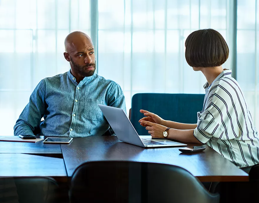 Woman working on a laptop and talking to a man