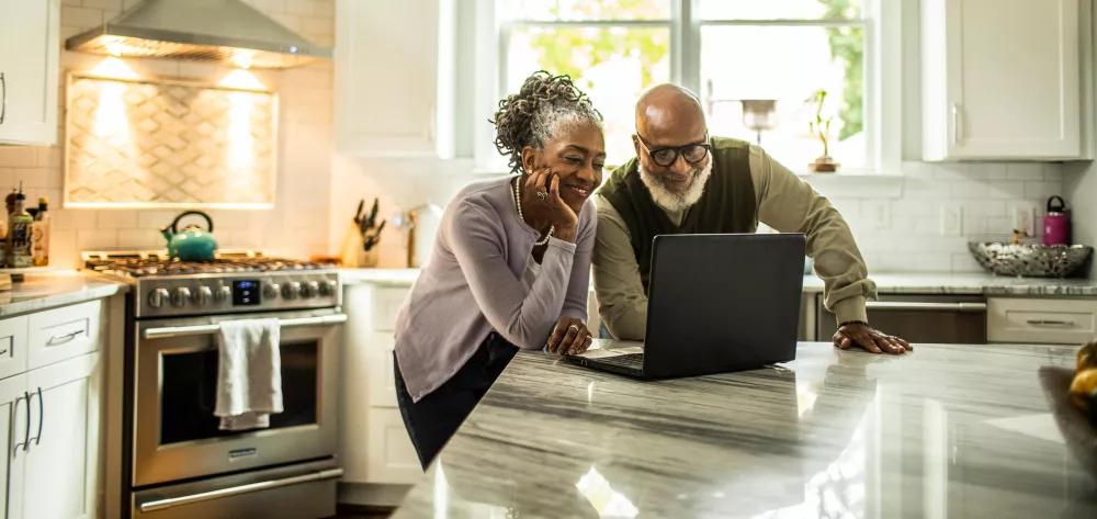 A couple in their kitchen looking at a laptop