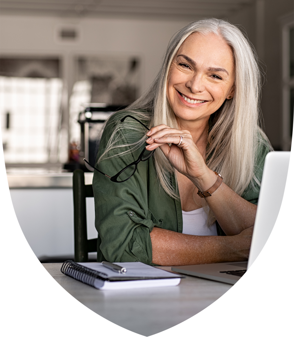 Close up of a woman holding her glasses and sitting at a laptop