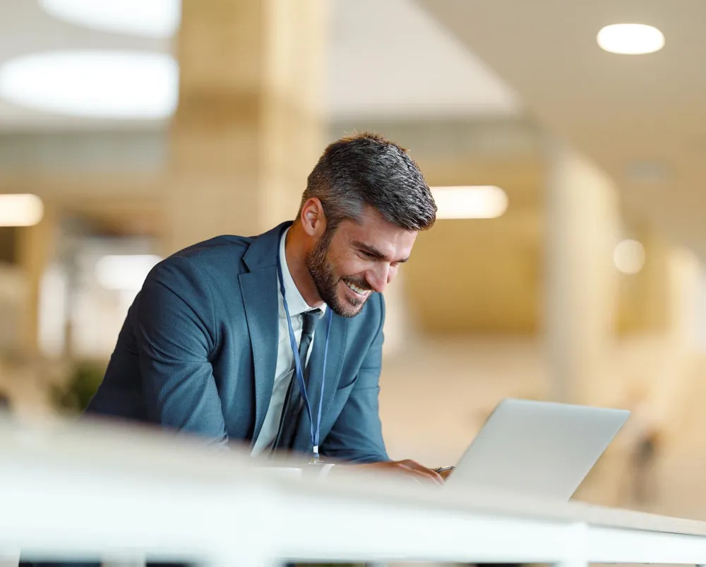 Man dressed in a suit smiling while looking at his laptop